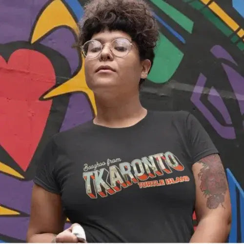 Person wearing a black t-shirt with colorful text in front of a vibrant graffiti wall.