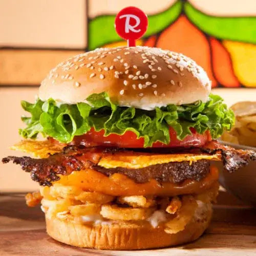 Stacked cheeseburger with lettuce, tomato, bacon, and crispy onions from Canadian-owned Ricky’s All Day Grill