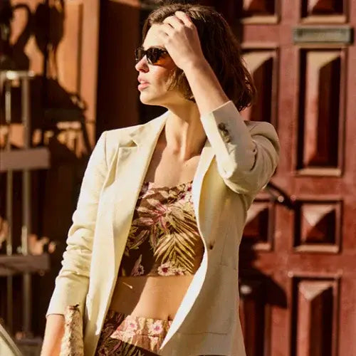 A stylish woman wearing sunglasses and a cream blazer over a floral print crop top and matching skirt. 