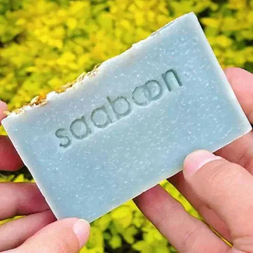 Bar of soap with 'saaboon' branding held in hands against a blurred natural background
