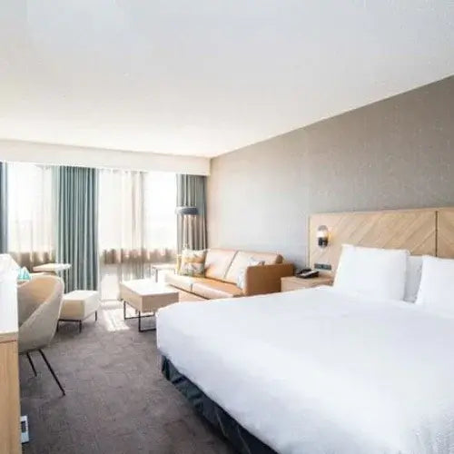 Modern hotel room with king bed, sofa seating area, and large windows with natural light
