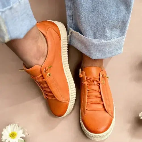 Orange sneakers with white soles worn by a person, on a neutral background.