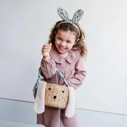 Child wearing bunny ears and holding a woven bag with a face design against a white background