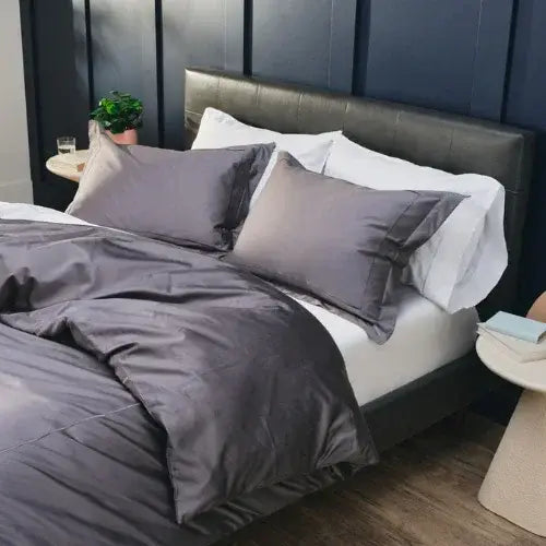 Bed with gray bedding and pillows against a dark paneled wall.