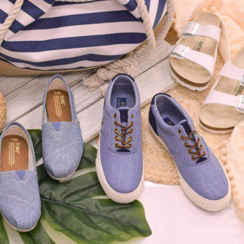 SoftMoc summer shoe display featuring denim slip-ons, canvas lace-up sneakers, and white sandals with a striped beach bag