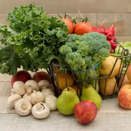 Fresh assorted produce including leafy greens, tomatoes, broccoli, potatoes, mushrooms, pears, and apples in a wire basket