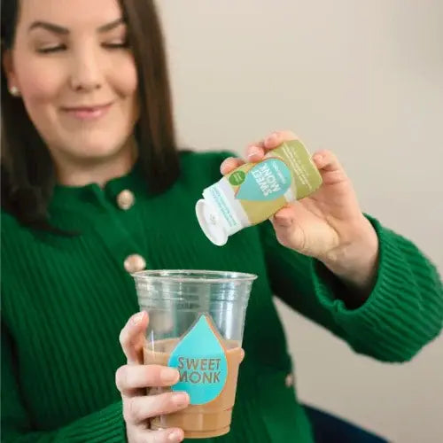 Person adding sweetener to a drink using a bottle labelled 'Sweet Monk'.