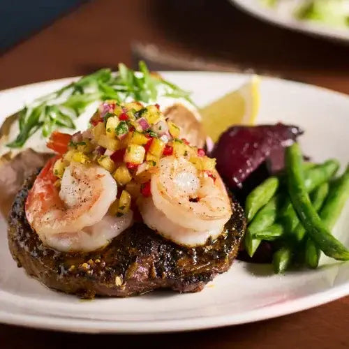 Plate of grilled shrimp on a bed of greens with a side of green beans and lemon wedge.