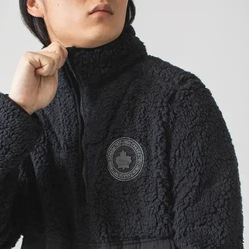 Person wearing a black fleece jacket with a logo on a plain background