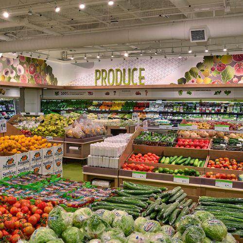 Colourful produce section at T&T Supermarket with neatly arranged fresh fruits and vegetables under a large 'PRODUCE' sign and illustrated wall mural.