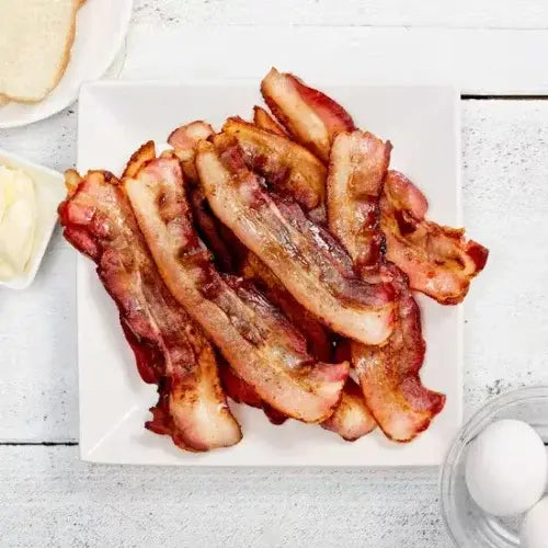 Bacon strips on a white plate with a light wooden background