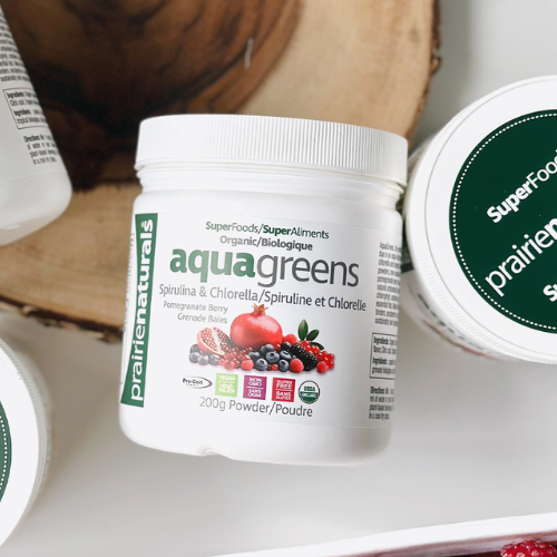 Container of aqua greens powder with a wooden surface in the background