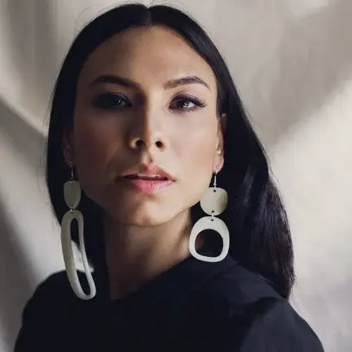 Woman wearing large white earrings against a neutral background