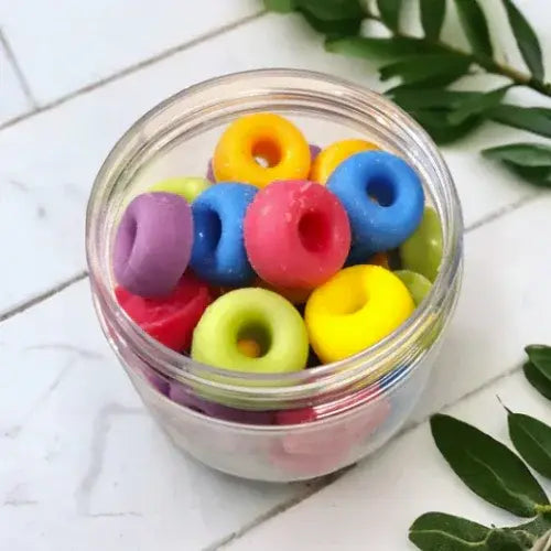 Jar filled with colorful rubber bands on a white surface with green leaves.
