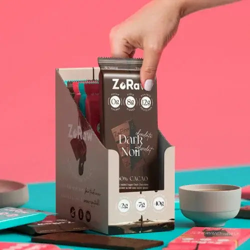 Hand reaching for a Zora chocolate bar packaging against a pink and blue background