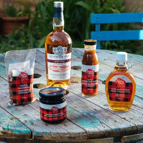 Collection of Acadian Maple maple syrup products on a wooden table outdoors.