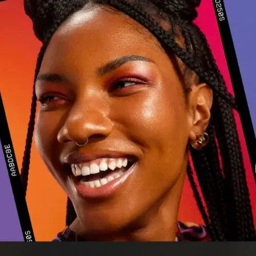 Confident woman with glowing skin and bold eye makeup smiling against a vibrant orange and pink background – beauty and skincare inspiration