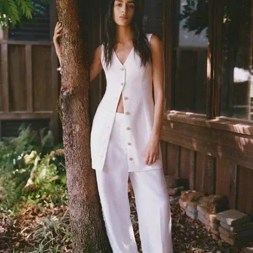 Woman wearing Aritzia sleeveless white linen vest and wide-leg pants, standing outdoors in natural summer light