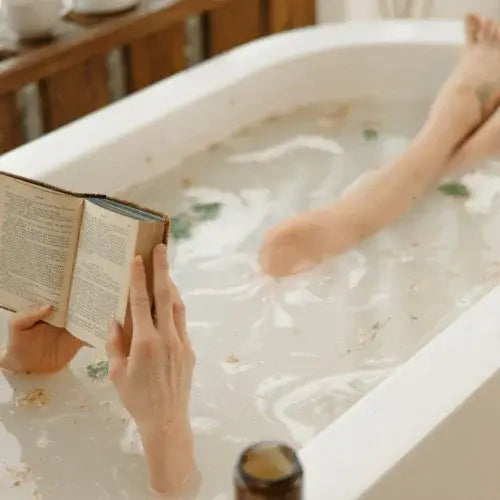 Person reading a book while soaking in a bathtub filled with water and herbs.