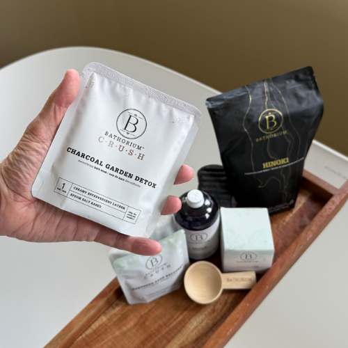 Hand holding a Bathorium Crush charcoal garden detox package with bath products on a tray.