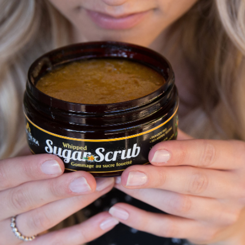 Person holding a jar of whipped sugar scrub with a blurred background