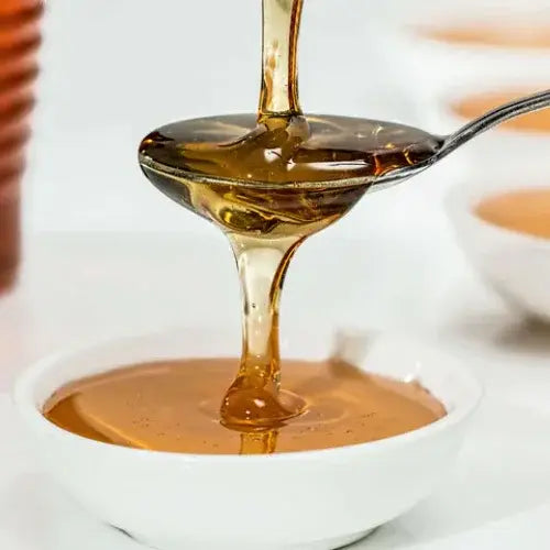Honey being dripped from a spoon into a white bowl on a blurred background
