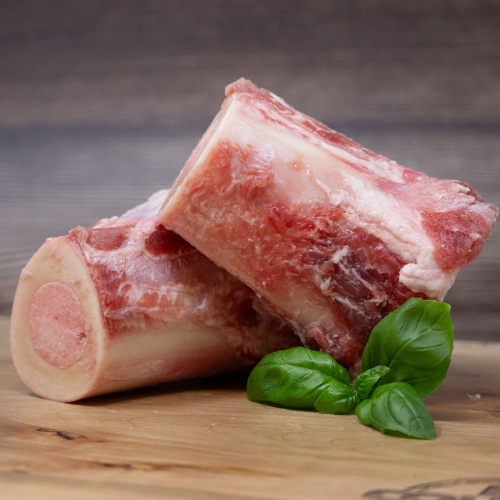 Two raw bones on a wooden surface with basil leaves