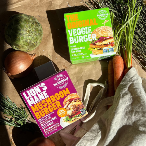 Two Big Mountain veggie burger packages with vegetables on a wooden surface