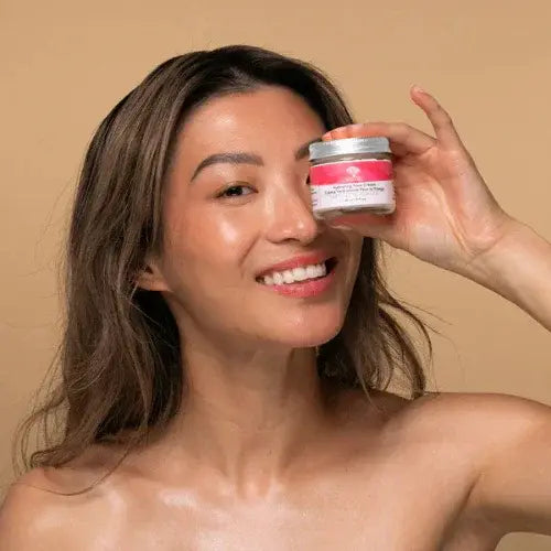 Smiling woman holding Birch Babe skin cream jar against a neutral background, showcasing natural skincare glow