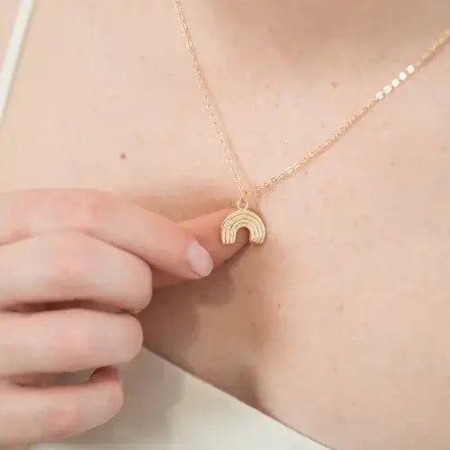woman wearing gold necklace with a rainbow pendant