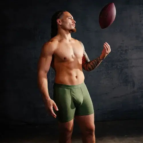 Man in green underwear holding a football against a dark background