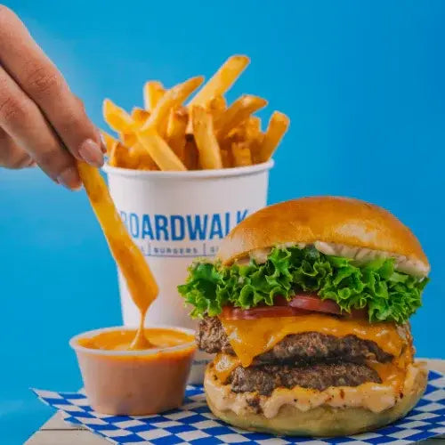 Hamburger with cheese, lettuce, and tomato on a bun with a side of fries and ketchup against a blue background.