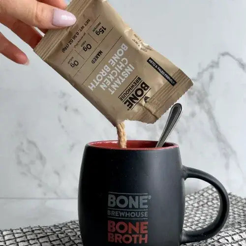 Person pouring Bone Brewhouse Bone Broth instant powder into a mug with a spoon.