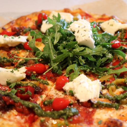 Close-up of a pizza with arugula, tomatoes, and cheese