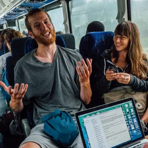 Two people on a bus, one using a laptop and the other looking at a phone.