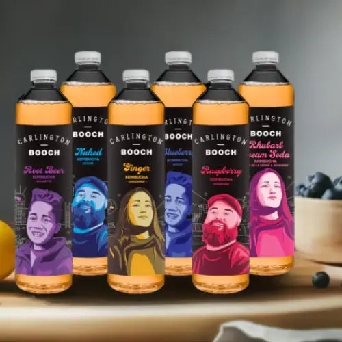 Carlington Booch soda bottles with colourful labels featuring people on a wooden surface.