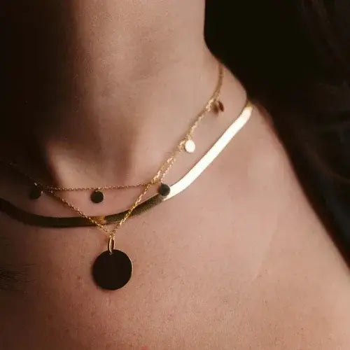 Close-up of a person wearing a gold necklace with circular pendants on a dark background