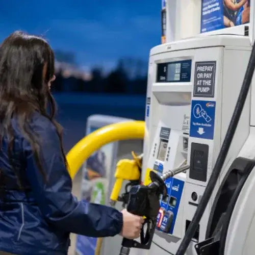 Person refueling a vehicle at a gas station with a blue sky background
