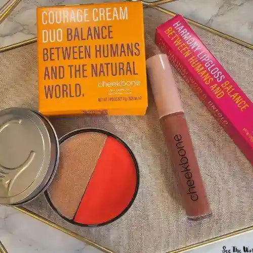 Makeup products including a compact, lip gloss, and powder with 'cheekbone' branding on a textured surface.