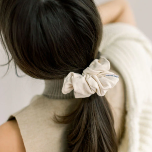 Person with a beige scrunchie in their hair against a neutral background