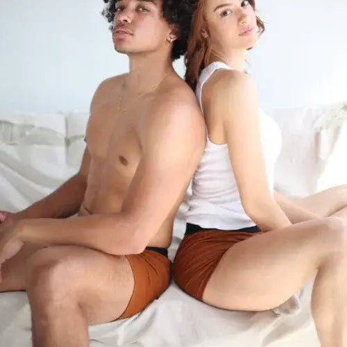 Two people sitting back-to-back on a white couch wearing brown shorts.