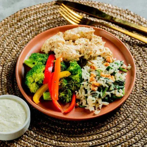 Plated meal with chicken, vegetables, and rice on a woven mat