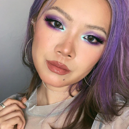 Person with purple hair and colourful makeup against a neutral background