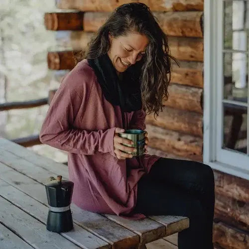 Woman sitting on a wooden bench holding a mug in front of a wooden cabin.