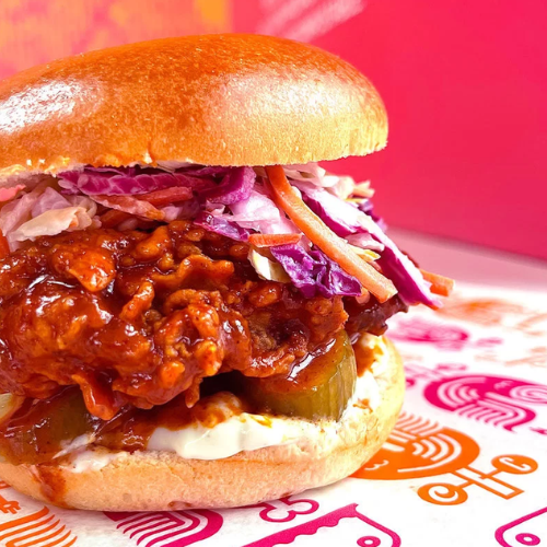 Close-up of a sandwich with chicken, coleslaw, and pickles on a colorful background
