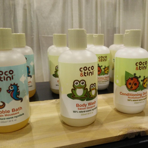 Bottles of coco & tini products on a wooden surface with a neutral background
