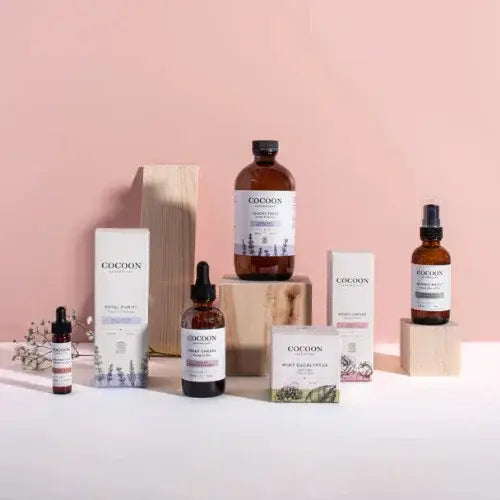 Cocoon Apothecary skincare products displayed on wooden blocks against a pink background