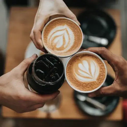 Three people toasting with lattes and iced coffee featuring latte art at a Canadian café