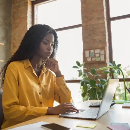 Focused young Black woman working on laptop in modern office with natural light