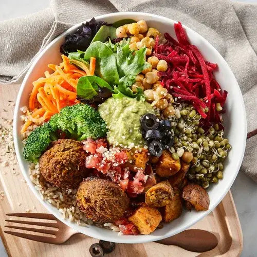 Vegan salad bowl with falafel, vegetables, and chickpeas on a wooden cutting board.